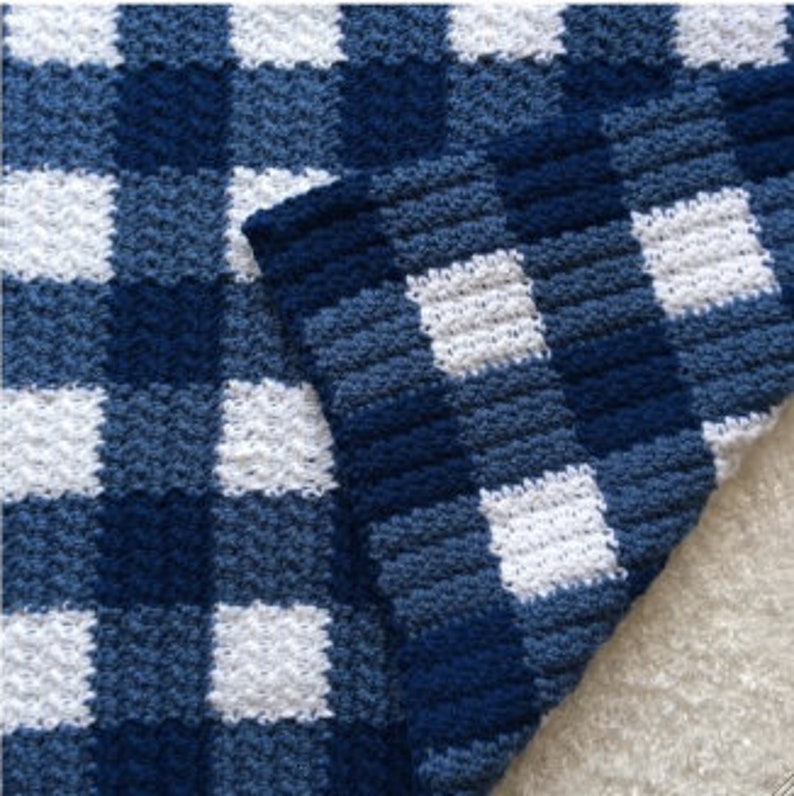 May include: A blue and white checkered crochet blanket with a textured pattern. The blanket is made with soft yarn and has a cozy feel.
