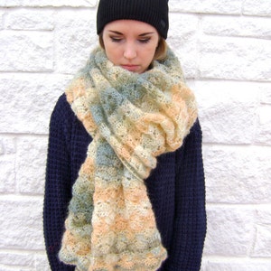 May include: A woman wearing a black beanie and a blue sweater with a light blue and peach colored knitted scarf.