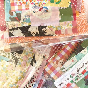 Puede incluir: Una colección de retales de tela en varios patrones y colores, incluyendo estampados florales, de cuadros y novedosos. Las telas están empaquetadas en plástico transparente. Algunos retales presentan ilustraciones de niños, animales y frutas. La estética general es vintage y caprichosa.