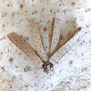 Op de afbeelding: Vier beige stoffen sleutelhangers met rode sterpatronen en zilveren sleutelringen.