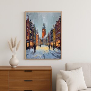 May include: A framed painting depicts a snowy street scene with buildings and a central tower. The artwork features a palette of blues, oranges, and yellows, with figures walking along the snow-covered street. The painting is displayed above a wooden cabinet.