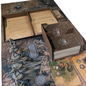 Könnte beinhalten: Brettspiel-Setup mit einer detaillierten Spielmatte mit einer Fantasy-Landschaft. Enthält Miniaturfiguren, Kartendecks und Karton-Aufbewahrungskomponenten. Die Karten haben Illustrationen von Charakteren und Szenen.
