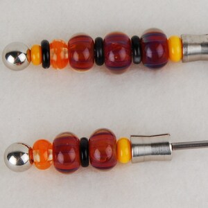May include: Two close-up images of a silver metal rod with colorful glass beads. The beads are orange, yellow, red, and purple. The rod has a metal tip on each end.