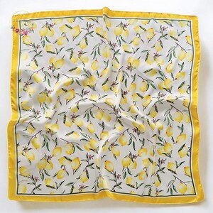 May include: Square silk scarf with a lemon pattern. The scarf features a white background with yellow lemons and green leaves. It has a yellow border with a thin green line.
