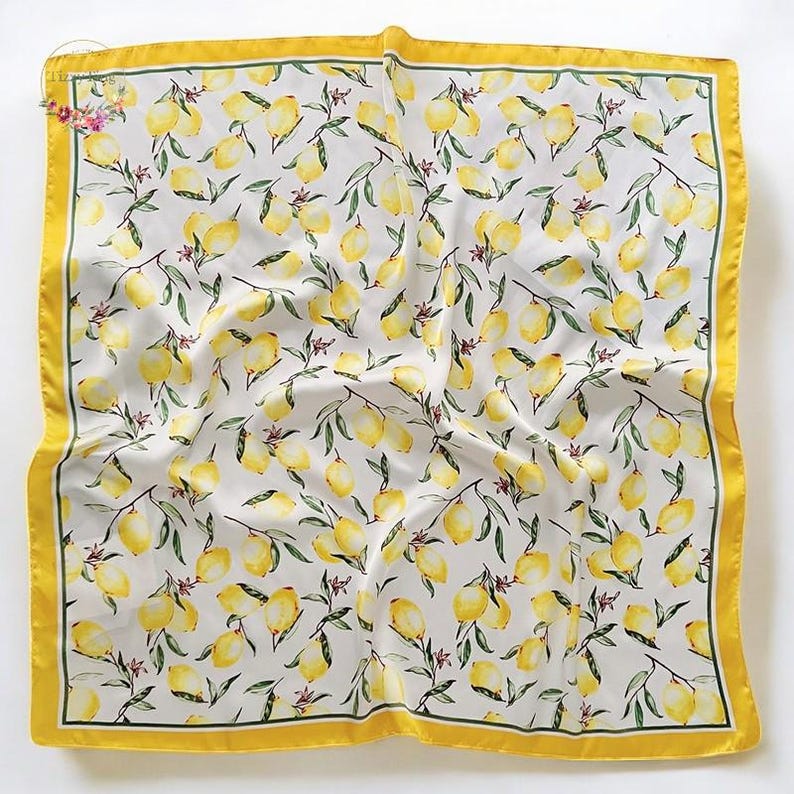 May include: Square silk scarf with a lemon pattern. The scarf features a white background with yellow lemons and green leaves. It has a yellow border with a thin green line.