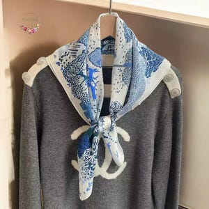 Puede incluir: Un suéter gris con un logotipo bordado en blanco y una bufanda con estampado azul y blanco atada alrededor del cuello.