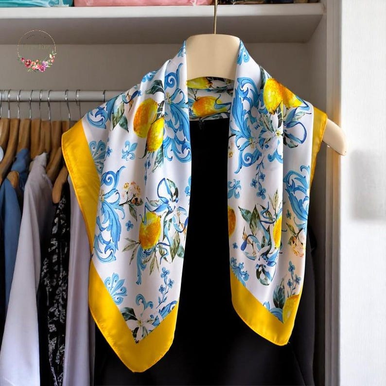 May include: A white silk scarf with a yellow border and a lemon print. The scarf features blue and white floral designs and lemons on a white background.