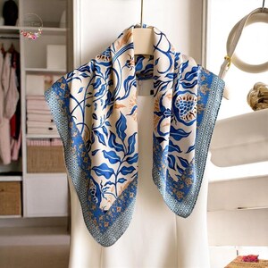 May include: A white silk scarf with a blue and gold floral pattern. The scarf is folded in half and draped over a white hanger.