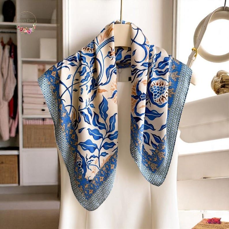 May include: A white silk scarf with a blue and gold floral pattern. The scarf is folded in half and draped over a white hanger.