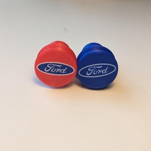 May include: Two round, plastic valve stem caps with the Ford logo. One cap is red and the other is blue.