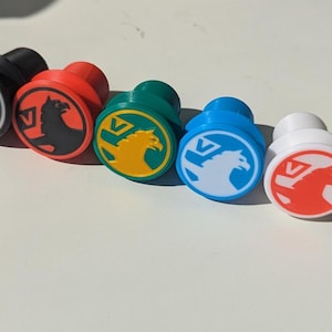 May include: Five decorative knobs in a row, each with a different colour: black, red, green, blue, and white. Each knob has a circular emblem with a stylised animal design.