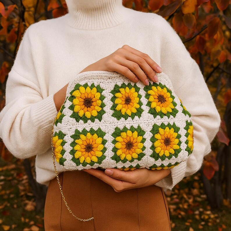 May include: A cream-colored crochet clutch featuring a sunflower pattern. The bag has a gold chain strap and is made with yellow, green, and brown yarn. The sunflower design is repeated across the front of the bag.