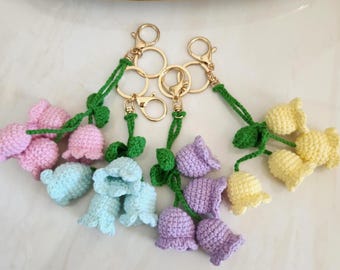 May include: A collection of handmade crochet flower keychains in various pastel colors, including pink, blue, purple, and yellow. Each keychain features a gold-colored clasp and green stem and leaves.