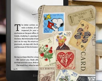 May include: A black e-reader displaying text on its screen, positioned next to a protective cover featuring a collage of vintage postage stamps, a playing card, and postal markings. The stamps include illustrations of Snoopy, flowers, cherries, a turtle, and a heart.