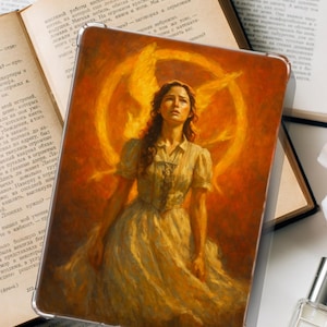 May include: A tablet case with a painting of a woman in a light dress, with a golden halo and a warm orange background. The case is on open books. The artwork is reminiscent of a classical style.