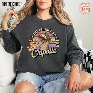 May include: Dark gray Comfort Colors sweatshirt with a colorful graphic that says "It's the perfect day for Chipotle." The graphic features a burrito, a sombrero, and a sunset design.