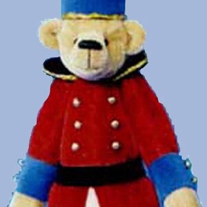 May include: A plush toy bear dressed as a toy soldier. The bear is wearing a red jacket with gold buttons, a blue hat with a gold trim, and black boots. The bear is holding a toy gun in its right paw. The bear is standing on a white background. Essential Bear is printed on the bottom of the image.