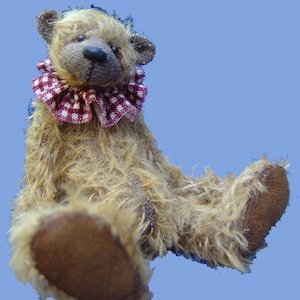 May include: A brown teddy bear with a red and white checkered collar. The bear is sitting with its legs outstretched and its paws are visible.