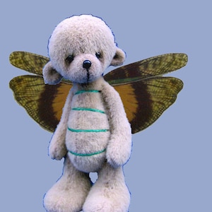 May include: A light gray teddy bear with green stripes on its torso and a pair of brown and yellow butterfly wings. The bear is standing on a light blue background. The text "Essential Bears" is at the bottom of the image.