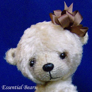 May include: A small, cream-colored teddy bear with a brown bow on its head. The bear has black eyes and a black nose. The bear is looking at the camera.