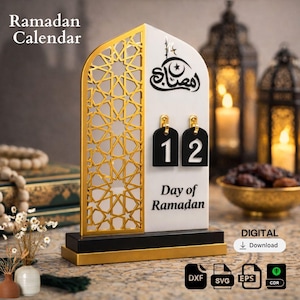 Puede incluir: Calendario del Ramadán con un diseño dorado y blanco. El calendario presenta un patrón de celosía dorada decorativa en un lado y muestra el día con etiquetas numéricas en blanco y negro. La base es negra y dorada, con el texto "Day of Ramadan".