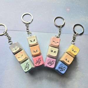 May include: Keyrings with stacked, colourful keycaps featuring cartoon animal faces and abstract designs. Each keyring has a silver ring and chain. The keycaps are in shades of grey, peach, pink, yellow, and blue.