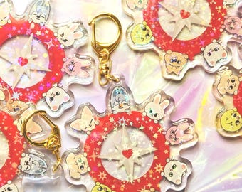 May include: Clear acrylic keyrings with a red and white compass design, surrounded by cartoon animal characters. Each keyring has a gold-coloured clasp. The compass design features a heart and starburst pattern.