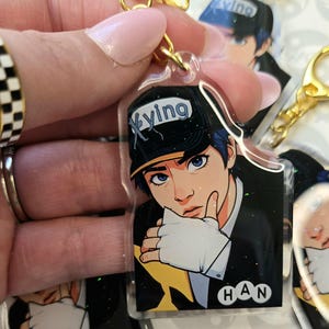 May include: Clear acrylic keychain featuring a stylized anime-style illustration of a person with blue hair and eyes, wearing a black cap with the word "Xying". The keychain has a gold-colored clasp and the name "HAN" is printed on the bottom.