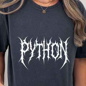 Peut inclure: T-shirt bleu marine foncé avec le mot "PYTHON" en blanc, dans une police gothique stylisée. Le t-shirt à manches courtes a un col rond. Le texte est l'élément principal du design.