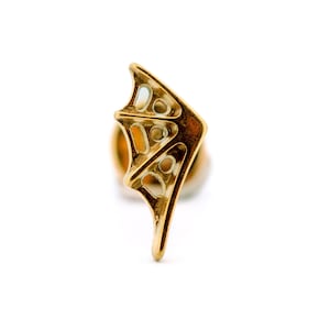 Op de afbeelding: Een goudkleurige oorbel met een vleugelachtig ontwerp. De oorbel heeft een opengewerkt patroon met afgeronde uitsparingen. De vleugelvorm heeft een puntige punt en een gebogen rand, wat een delicate en elegante uitstraling creëert.