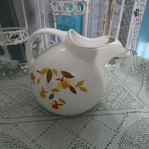 May include: White ceramic pitcher with a brown, yellow, and orange floral pattern. The pitcher has a wide mouth and a handle.