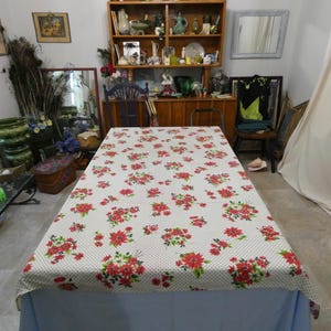 May include: A rectangular tablecloth with a white background and a pattern of red floral bouquets and small black polka dots. The tablecloth is covering a light blue table.