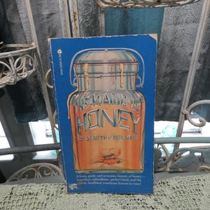 May include: A blue book with the title "The Magic of Honey" by Dorothy V. Perlman. The cover features a vintage illustration of a honey jar with a bee and a flower.