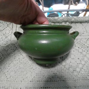 May include: A small, green ceramic pot with two handles. The pot is glazed and has a smooth finish.
