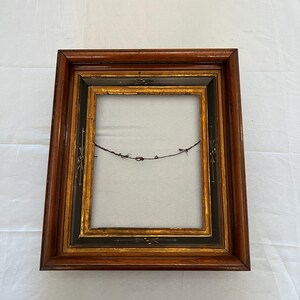 May include: A rectangular wooden picture frame with a dark brown finish. The frame has a gold inner border and black accents. A wire is strung across the back of the frame.