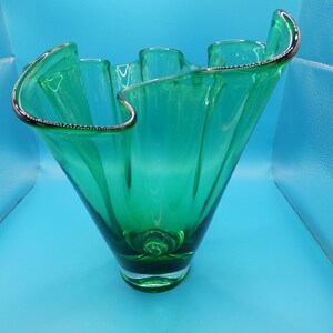 May include: A green glass vase with a ruffled rim and a silver-colored trim. The vase has a flared shape and a rounded base. The glass is transparent, allowing light to pass through. The vase is a decorative item.