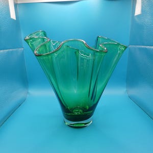 May include: A vibrant green glass vase with a ruffled rim and a silver trim. The vase has a flared shape and a clear base. The glass is a rich emerald green color. The vase is likely used for decorative purposes.
