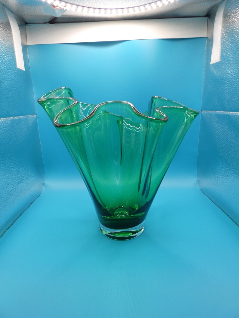 May include: A vibrant green glass vase with a ruffled rim and a silver trim. The vase has a flared shape and a clear base. The glass is a rich emerald green color. The vase is likely used for decorative purposes.