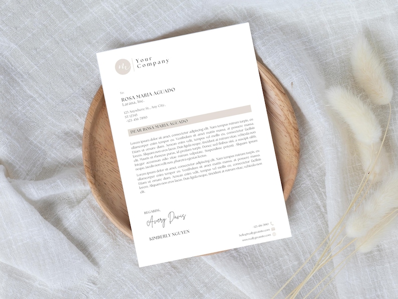 以下が含まれることがあります： 「Your Company」というテキストとロゴが入ったレターヘッドが木製のプレートに表示されています。手紙はRosa Maria Aguado宛てで、Avery DavisとKimberly Nguyenが署名しています。背景は白い布です。