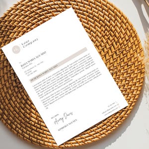 以下が含まれることがあります： 「Your Company」の文字と「ROSA MARIA AGUADO」の名前が書かれたレターヘッドが、織り込まれた籐のプレースマットの上に表示されています。手紙には、正式な挨拶と結び、署名が含まれています。背景は薄いベージュ色です。