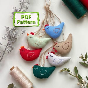May include: A collection of handmade fabric chicken ornaments in various colors, including red, blue, green, and beige, each with a stitched design. The image also shows spools of thread and the text "PDF Pattern". These ornaments are likely for crafting or home decor.