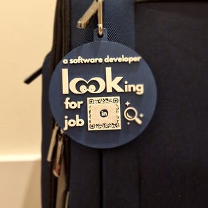 May include: A blue round tag with the text "a software developer looking for job" and a LinkedIn logo with a QR code. The tag is attached to a blue zippered bag.