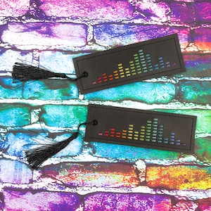 Op de afbeelding: Twee zwarte leren bladwijzers met regenboogkleurige equalizer-ontwerpen. Elke bladwijzer heeft een zwarte kwast.