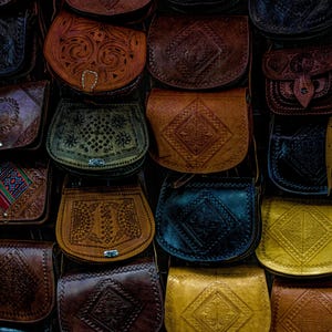 Può includere: Una collezione di borse e borsette in pelle di vari colori e design. Le borse sono tutte in pelle marrone e hanno motivi e disegni intricati. Alcune delle borse hanno chiusure e fibbie in metallo.