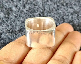 Könnte beinhalten: Ein quadratischer, polierter Silberring. Der Ring hat ein minimalistisches Design und eine glatte, reflektierende Oberfläche. Das Innere des Rings ist sichtbar, mit der Markierung "925" im Inneren. Der Ring wird in einer Hand gehalten.