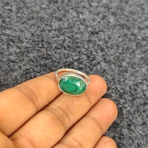 May include: A silver ring featuring an oval-cut, emerald-green gemstone. The ring's band is a simple, polished silver, and the gemstone is set in a bezel setting. The ring is displayed on a neutral background.