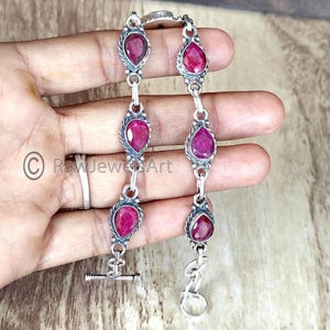 Puede incluir: Un brazalete de plata con cierre de palanca presenta seis piedras preciosas en forma de lágrima de rubí.