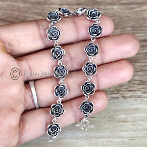 May include: A silver chain bracelet with black rose charms. The bracelet is made of sterling silver and features a delicate chain with a lobster clasp.