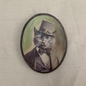 Pintura de gato con sombrero de estilo victoriano sobre panel de madera ovalado