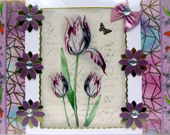 Puede incluir: Una tarjeta de felicitación decorativa con una pintura de acuarela de tulipanes morados y blancos. La tarjeta está adornada con acentos de flores moradas, un lazo rosa y una mariposa. El fondo tiene un diseño de guion vintage.